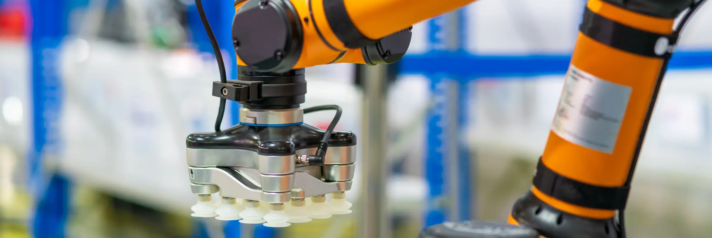 Orange and black industrial robotic arm with gripper handling white component in automated manufacturing facility.