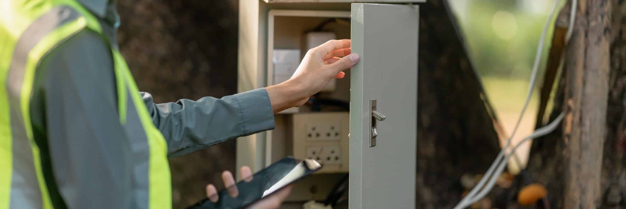 Electrical technician in safety vest inspecting a UL 508A certified control panel enclosure with tablet documentation on-site